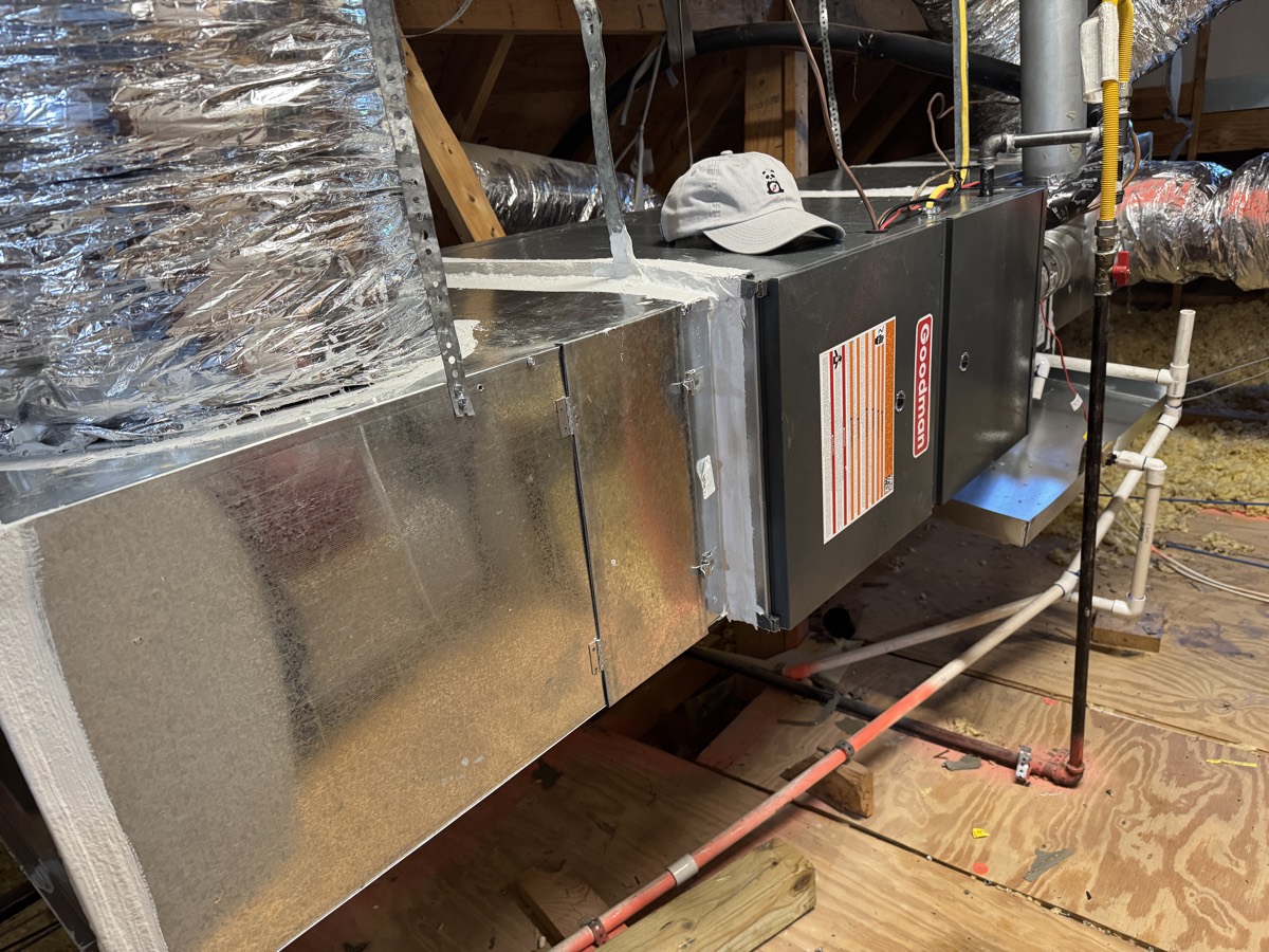Goodman gas furnace and air handler in an attic in Celina, TX, with the supply plenum, flex duct runs, gas line and condensate drain visible during a seasonal heating tune-up