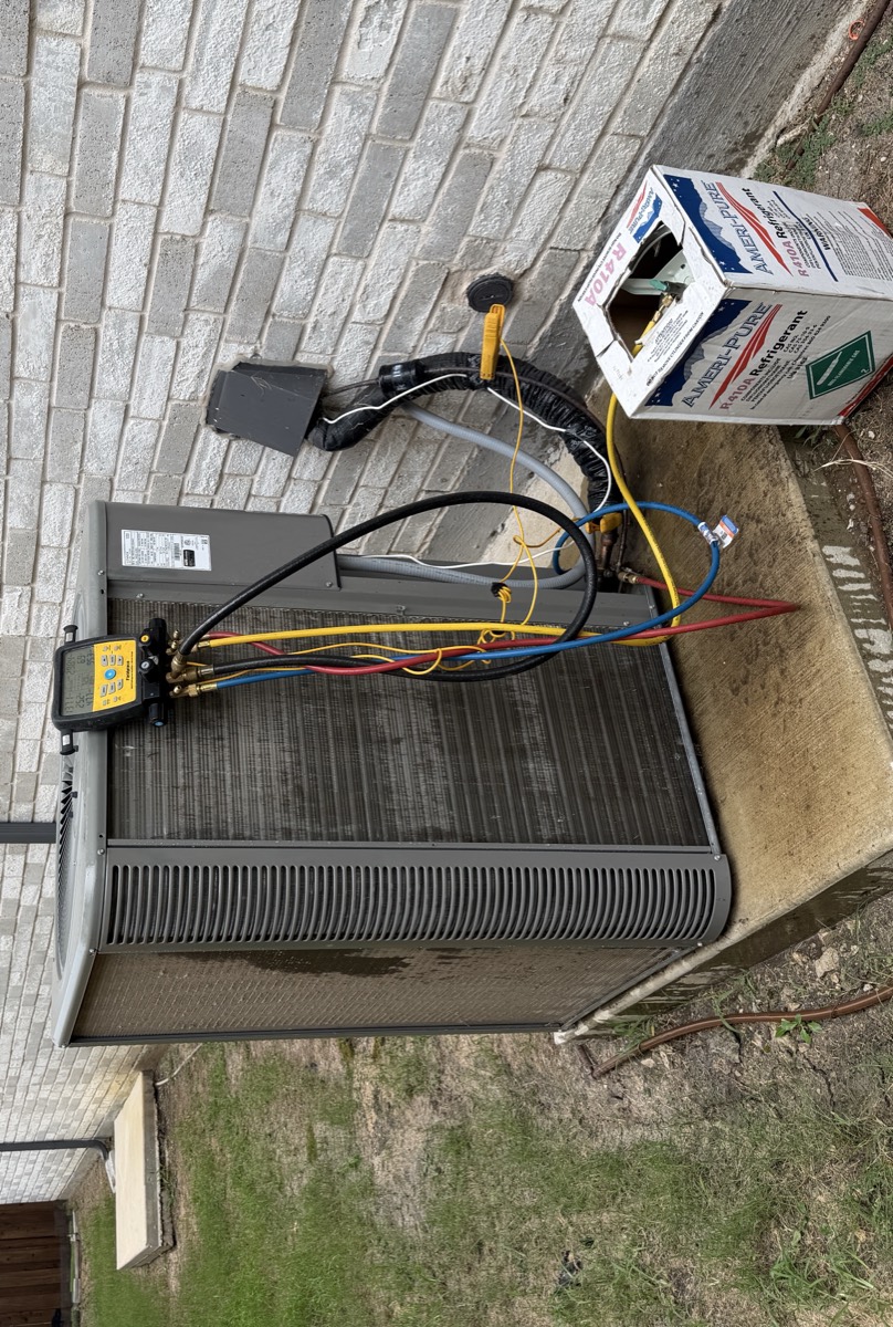 Heat pump repair on an outdoor unit in Celina, TX, with digital manifold gauges connected at the service ports, R-410A refrigerant on site and the electrical disconnect open