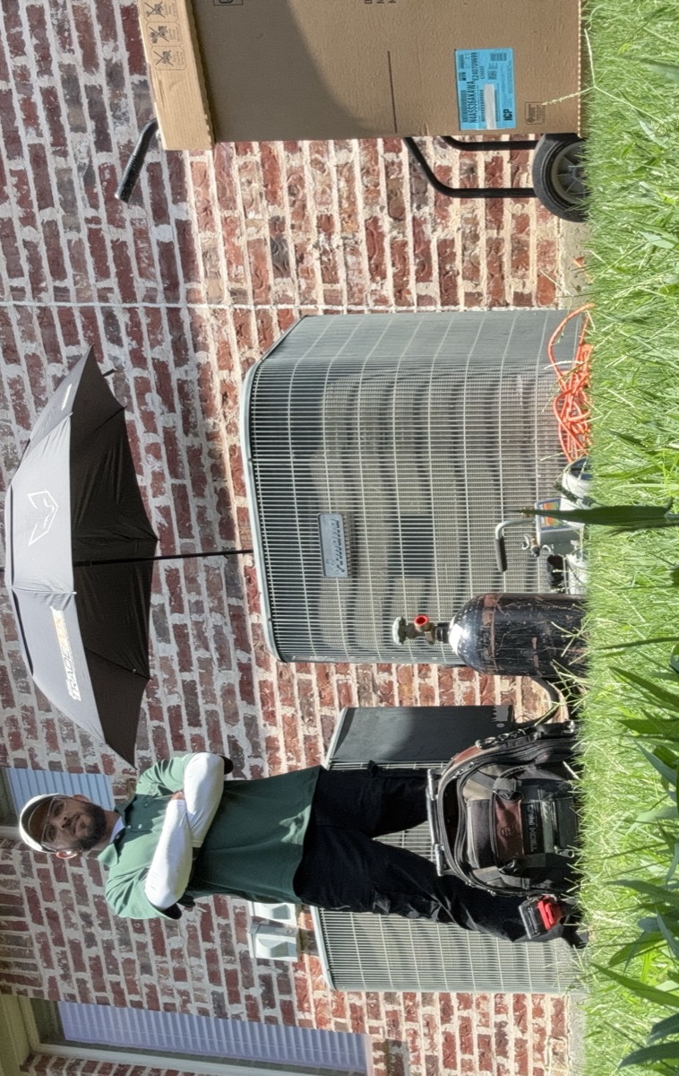 Panda Heating and Cooling technician on a service call in Celina, TX, standing beside the outdoor unit with the tool bag, nitrogen tank, vacuum pump and a new condenser on the hand truck