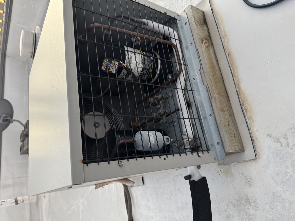 Walk-in cooler condensing unit opened for repair on a commercial rooftop, showing the compressor, receiver, condenser coil and copper line set